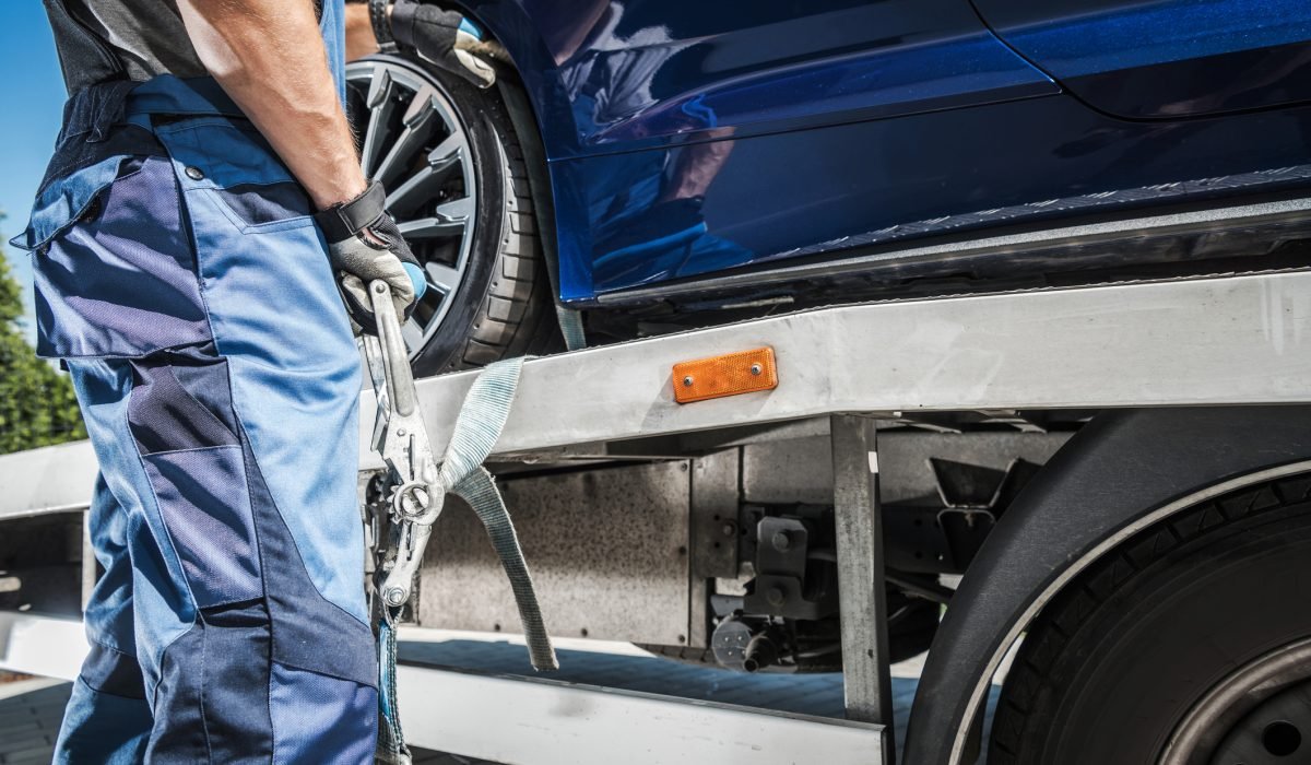 Male Worker Putting Transport Belts Around the Wheel of a Car on His Trailer to Secure It for Safe Carriage. Vehicle Transportation Theme.