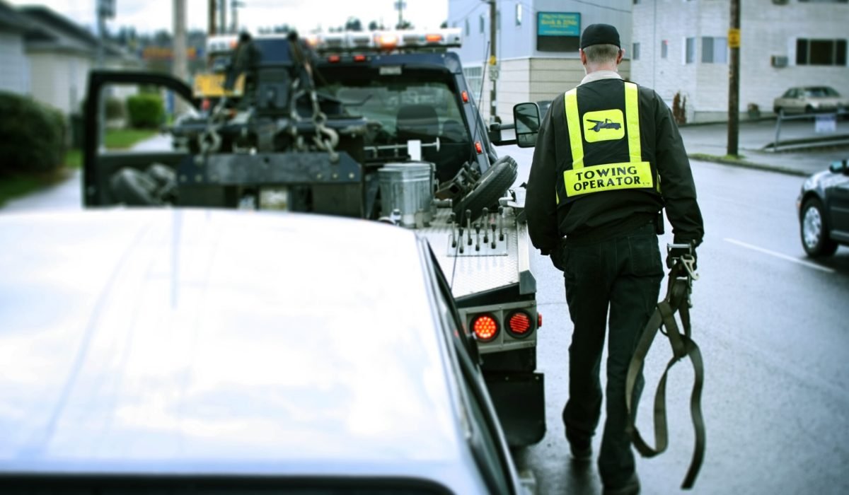 A road side assistance professional on the job hooking up a broken down car to his tow truck.  Horizontal with copy space.